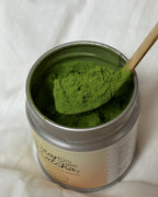 Canister of green powder on a wooden surface with a checkered cloth underneath